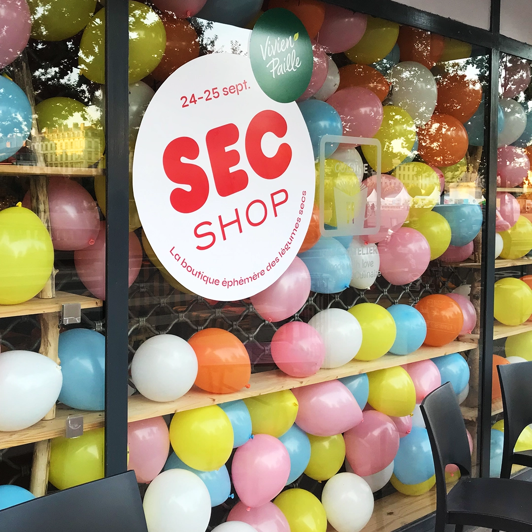 Scénographie commerciale et événementielle de la vitrine de la boutique éphémère 'Sec Shop' pour la marque 'Vivien Paille', décor éphémère, ballons colorés et vitrophanie